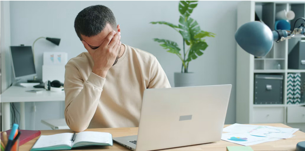 Tired man rubbing his face while working at a laptop, a common sign of high-functioning depression